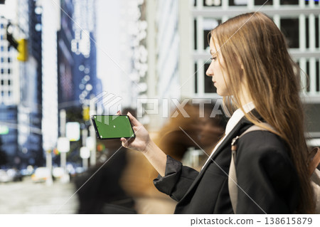 Horizontal mockup display on smartphone held by cool student girl with backpack, diverse pedestrian crowd walking along the busy metropolitan streets during morning commute. Horizontal mockup display on smartphone held by cool student girl with backpack, diverse pedestrian crowd walking along the busy metropolitan streets during morning commute. 138615879