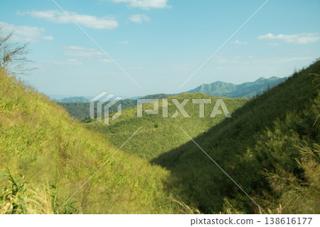 Green mountain valley with rolling hills under blue sky, peaceful natural landscape background with travel and wilderness concept. Green mountain valley with rolling hills under blue sky, peaceful natural landscape background with travel and wilderness concept. 138616177