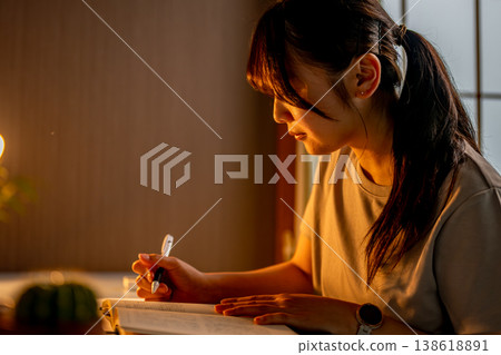 夜幕降臨，一位女子在房間裡手持一本書學習。 138618891