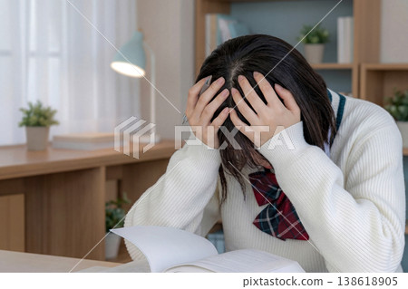 A shot of a female student in a school uniform holding her head in her hands at a desk. 138618905