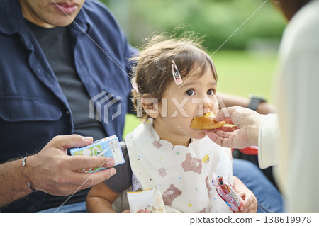 A toddler being fed by his father in the park 138619978