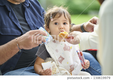 A toddler eating bread on his father's lap 138619979