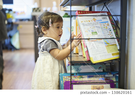 一個蹣跚學步的孩子從書架上拿起一本圖畫書。 一個蹣跚學步的孩子從書架上拿起一本圖畫書。 138620161