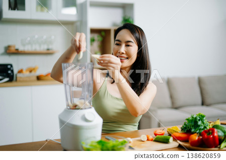 Smiling woman making healthy salad in modern kitchen with fresh greens, fruits, and blender. A clean eating and wellness lifestyle concept in a bright home Smiling woman making healthy salad in modern kitchen with fresh greens, fruits, and blender. A clean eating and wellness lifestyle concept in a bright home 138620859