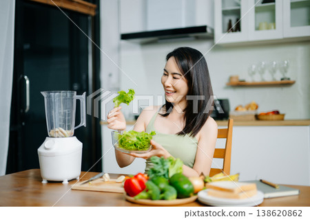 Smiling Asian woman cutting vegetables in a modern kitchen. Concept of healthy lifestyle, clean eating, vegan diet, organic nutrition, and wellness 138620862