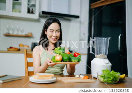 Happy Asian woman holding a plate of fresh vegetables and smiling in a modern kitchen. Concept of healthy lifestyle, clean eating, vegan diet, and organic nutrition 138620868