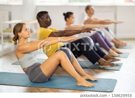 Young female Pilates instructor performing sit-ups with ball at group class Young female Pilates instructor performing sit-ups with ball at group class 138620958