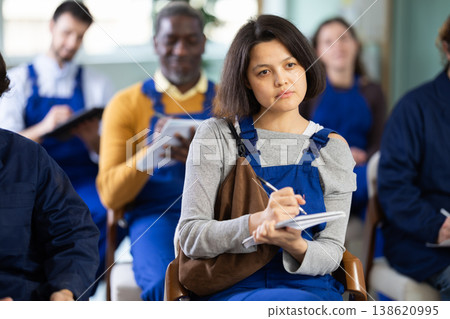 Young female worker listens and takes notes in lecture hall Young female worker listens and takes notes in lecture hall 138620995