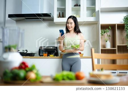 Healthy lifestyle concept of woman holding salad and smartphone at home kitchen. Diet, weight loss, fitness, nutrition and modern wellness routine Healthy lifestyle concept of woman holding salad and smartphone at home kitchen. Diet, weight loss, fitness, nutrition and modern wellness routine 138621133