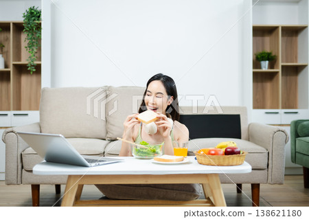 Happy woman enjoying healthy salad at home while using smartphone and headphones. Modern lifestyle, wellness, fitness, and digital living concept Happy woman enjoying healthy salad at home while using smartphone and headphones. Modern lifestyle, wellness, fitness, and digital living concept 138621180