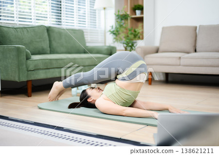 Asian woman practicing yoga and home workout in a bright living space. Healthy lifestyle, fitness, balance, and mindfulness concept with calm and modern atmosphere. Asian woman practicing yoga and home workout in a bright living space. Healthy lifestyle, fitness, balance, and mindfulness concept with calm and modern atmosphere. 138621211