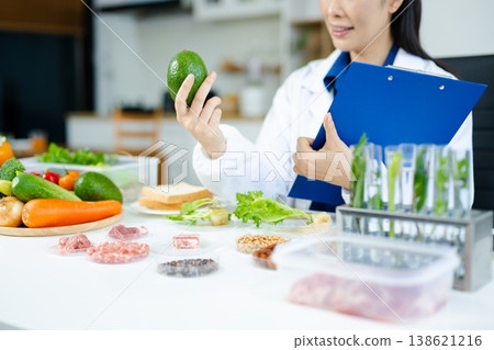 Nutritionist woman in lab coat analyzing vegetables, meat, grains in a modern food science lab. Healthy lifestyle, diet research, clinical testing Nutritionist woman in lab coat analyzing vegetables, meat, grains in a modern food science lab. Healthy lifestyle, diet research, clinical testing 138621216