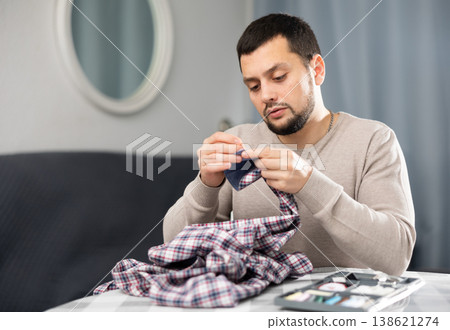 Man sewing button on shirt sleeve at home 138621274