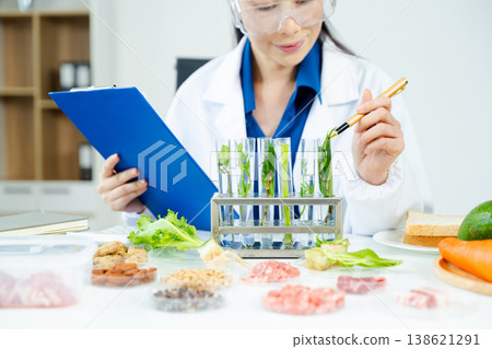 Nutritionist in lab coat and goggles holding test tube with green plant sample. Food safety, nutrition science, biotech, and clean health research concept. Nutritionist in lab coat and goggles holding test tube with green plant sample. Food safety, nutrition science, biotech, and clean health research concept. 138621291