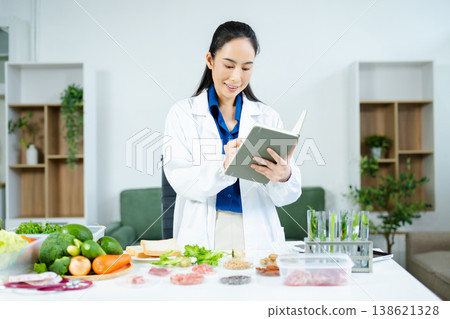 Female nutritionist in lab coat analyzing food and writing in notebook. Healthy eating, organic testing, and nutrition science in a clean lab. Female nutritionist in lab coat analyzing food and writing in notebook. Healthy eating, organic testing, and nutrition science in a clean lab. 138621328