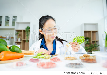 Female food scientist in lab coat and goggles analyzing fresh lettuce roots. Organic farming, hydroponics, nutrition science, and healthy research lab. Female food scientist in lab coat and goggles analyzing fresh lettuce roots. Organic farming, hydroponics, nutrition science, and healthy research lab. 138621329