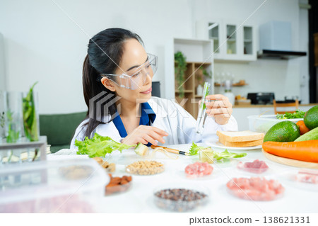 Female nutritionist in lab coat and goggles inspecting green plant in test tube. Food research, health, nutrition science, and biotech lab concept. Real people in clinical setting. Female nutritionist in lab coat and goggles inspecting green plant in test tube. Food research, health, nutrition science, and biotech lab concept. Real people in clinical setting. 138621331