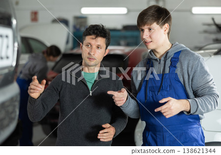 Adult car owner discusses with a young auto mechanic the cost and time of car repairs at car service center 138621344