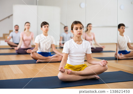 Preteen girl sitting in lotus position during yoga class with family Preteen girl sitting in lotus position during yoga class with family 138621450