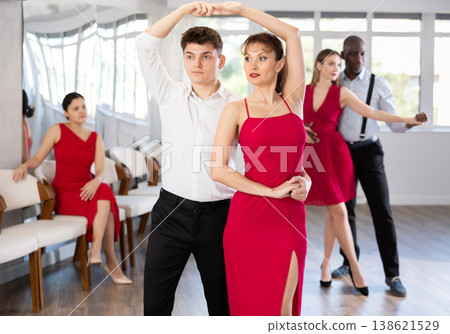 Happy young woman dressed in red dress with man in elegant clothes dancing bachata in ballroom dance class Happy young woman dressed in red dress with man in elegant clothes dancing bachata in ballroom dance class 138621529