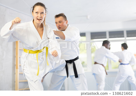 Middle-aged woman attendee of karate classes fighting with her opponent in sports hall Middle-aged woman attendee of karate classes fighting with her opponent in sports hall 138621602