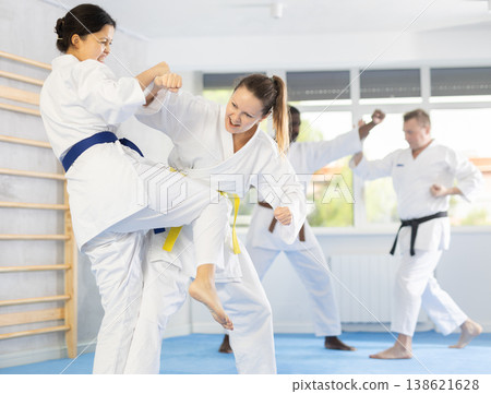 Middle-aged woman attendee of karate classes fighting with her opponent in sports hall Middle-aged woman attendee of karate classes fighting with her opponent in sports hall 138621628