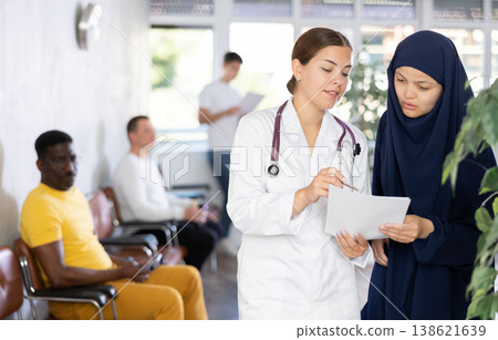 Young female doctor showing papers to Muslim woman in lobby of clinic 138621639