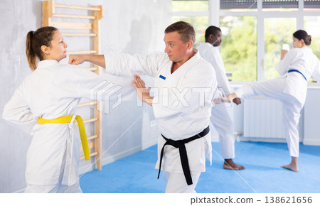 Woman and man in kimono sparring in gym during karate training Woman and man in kimono sparring in gym during karate training 138621656