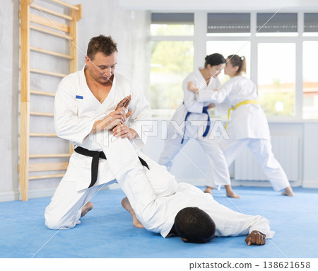 Judo or jiu-jitsu classes - two men practicing grabbing and throwing on sports mats under the guidance of trainer 138621658