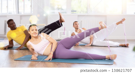 Pilates class - group of people of different nationalities doing leg stretches using resistance bands in gym 138621707