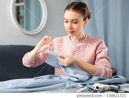 Young woman sewing on button at home 138621721
