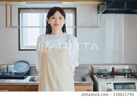 A woman in an apron smiling in the kitchen; an image of housework and cooking; a positive lifestyle scene. A woman in an apron smiling in the kitchen; an image of housework and cooking; a positive lifestyle scene. 138621740