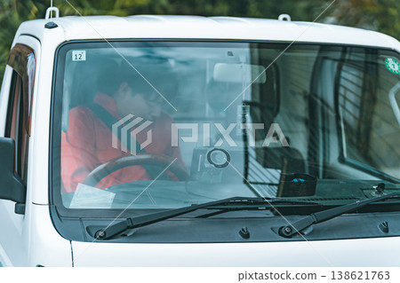 A man in overalls driving a light truck. 138621763