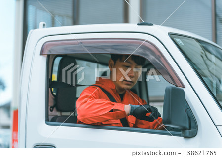 一名身穿工作服的男子駕駛著一輛輕型卡車。 一名身穿工作服的男子駕駛著一輛輕型卡車。 138621765