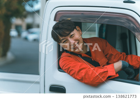 A man in overalls driving a light truck. 138621773