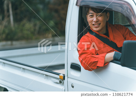 一名身穿工作服的男子駕駛著一輛輕型卡車。 138621774