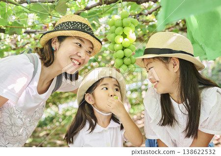 A close-up of a parent and child posing with a bunch of grapes. 138622532