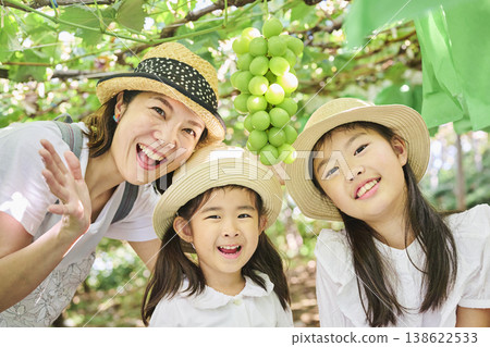 A portrait of a mother and daughter smiling, with bunches of Shine Muscat grapes. 138622533