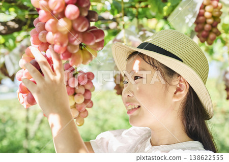 A girl picks up a bunch of red grapes. 138622555