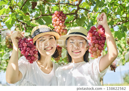 A mother and daughter holding up a bunch of red grapes. A mother and daughter holding up a bunch of red grapes. 138622562