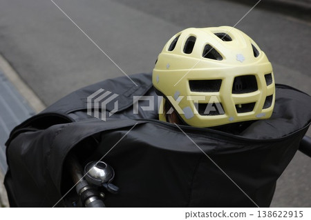 一個孩子背對著鏡頭,戴著頭盔,坐在自行車前籃裡的兒童座椅上,車籃上裝有車罩。 一個孩子背對著鏡頭,戴著頭盔,坐在自行車前籃裡的兒童座椅上,車籃上裝有車罩。 138622915
