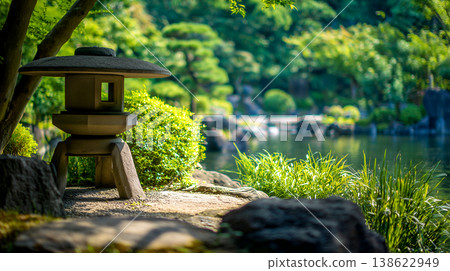 一座迷人的石燈籠放置在日式花園的池塘邊，周圍綠樹環繞，沐浴在初夏的自然光中。 138622949