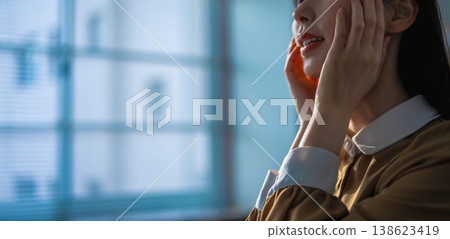 Close-up of a woman with her hand on her face by a window. Close-up of a woman with her hand on her face by a window. 138623419