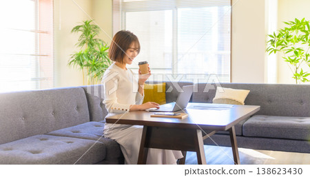 A woman uses her laptop at home while drinking coffee. 138623430
