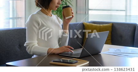 A woman drinks coffee while working on her PC at home. 138623431