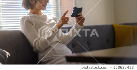 一位女士正在沙發上使用智慧型手機。 138623438