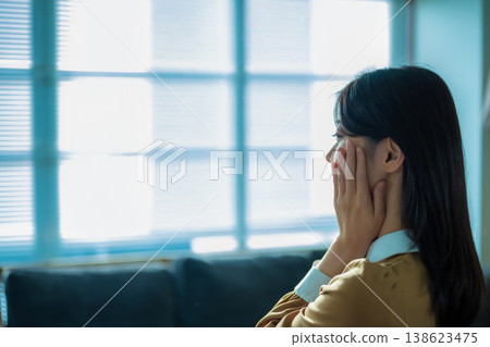 A woman with her hand on her face by the window. A woman with her hand on her face by the window. 138623475