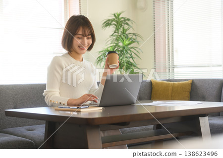 一位女士在家一邊喝咖啡一邊使用筆記型電腦。 一位女士在家一邊喝咖啡一邊使用筆記型電腦。 138623496