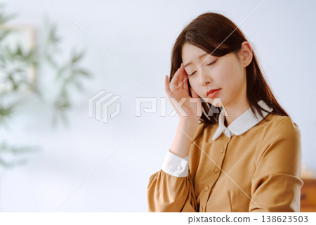 A woman puts her hand to her temple because she has a headache. A woman puts her hand to her temple because she has a headache. 138623503