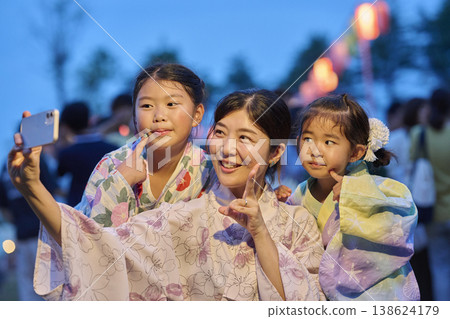 Mother and sisters making peace signs at a summer festival at dusk. 138624179